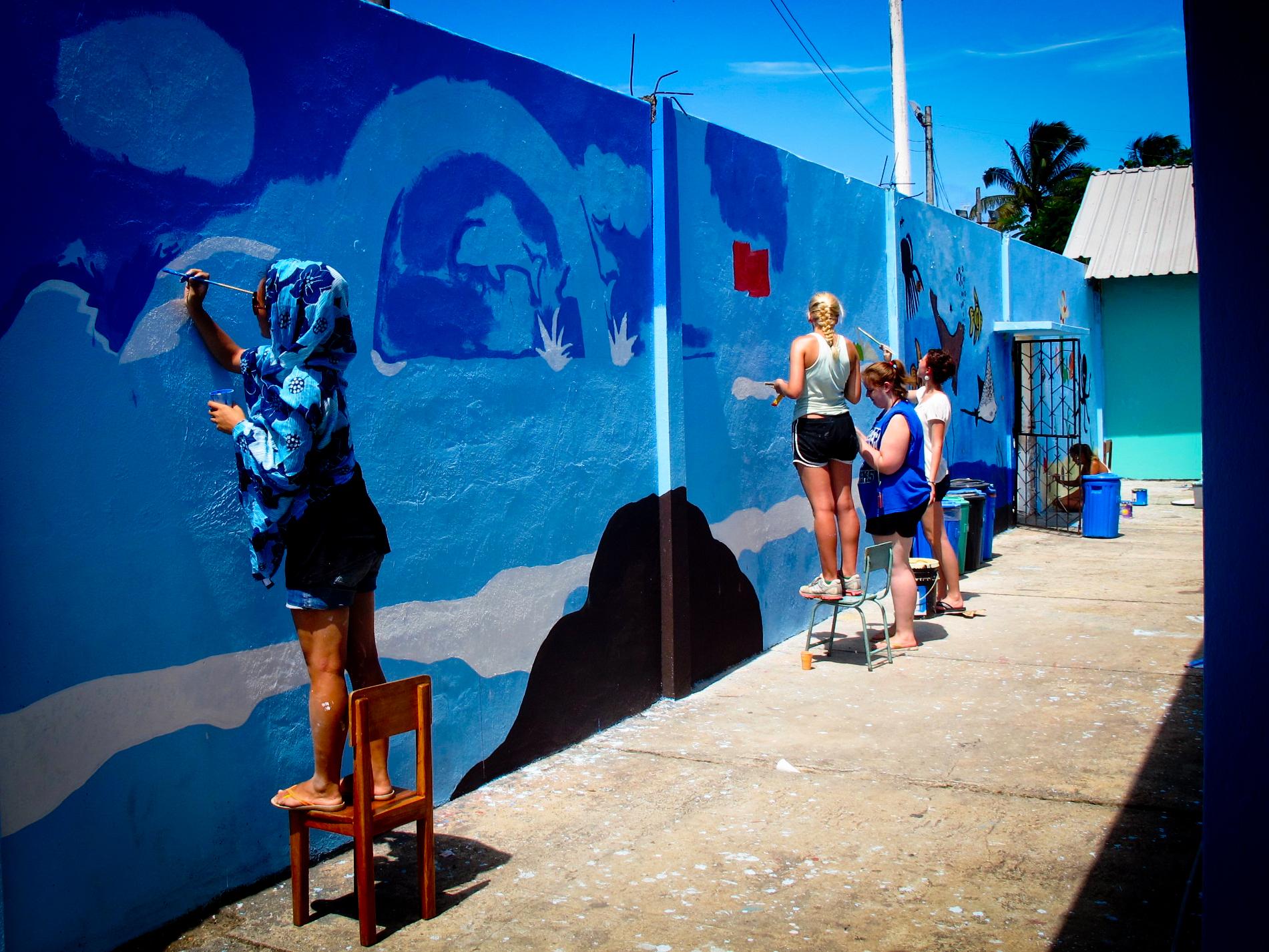 Projects Abroad volunteers in Ecuador paint a wall outside a care centre during their Childcare Project. Female volunteers working with children in Ecuador paint a wall blue to help improve the learning environment at a kindergarten.